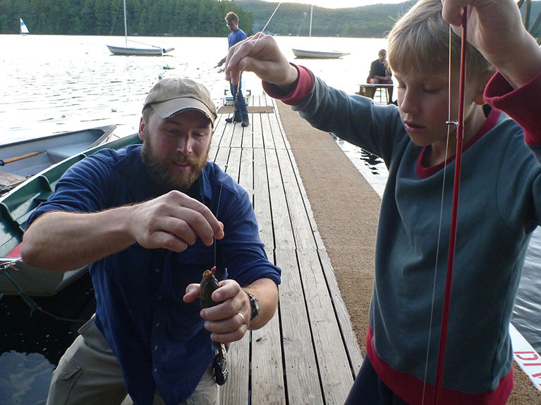 counselor showing camper how to take hook out of caught fish's mouth