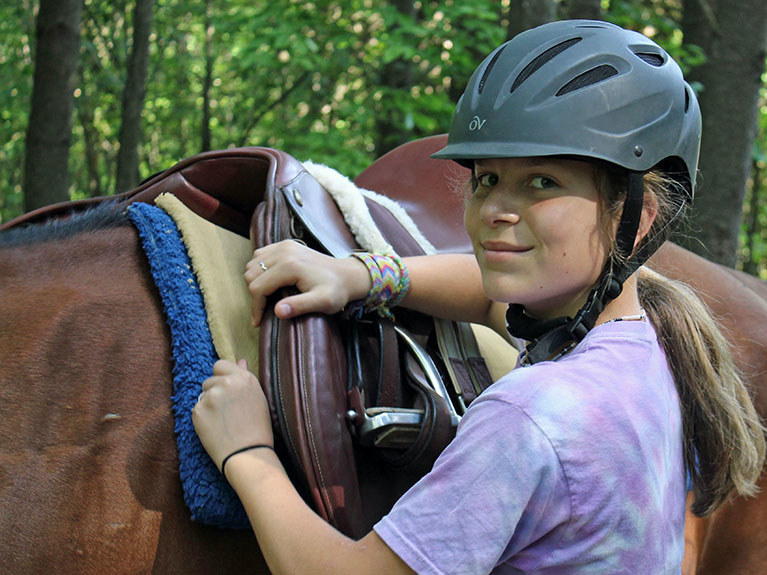 camper putting saddle on horse