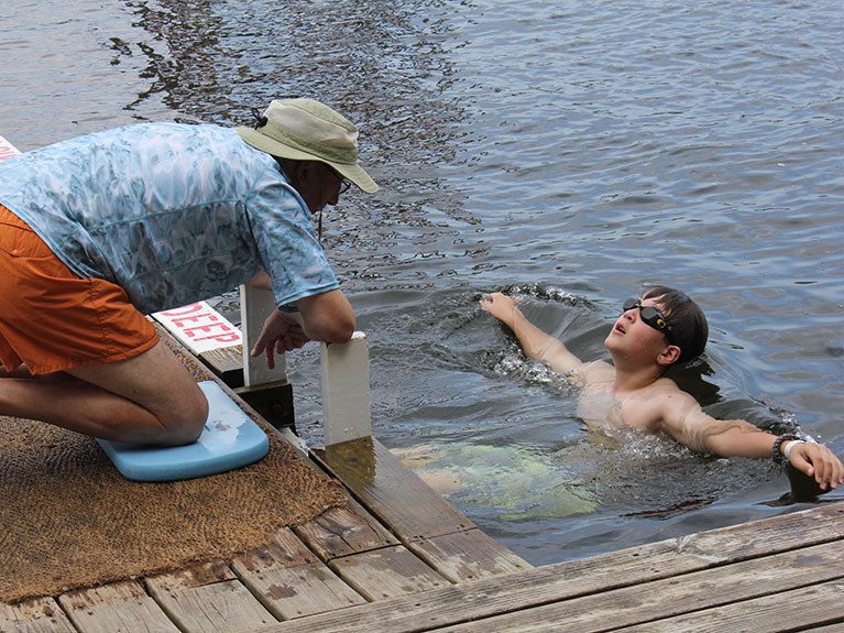 Instructor on dock teaching camper to swim