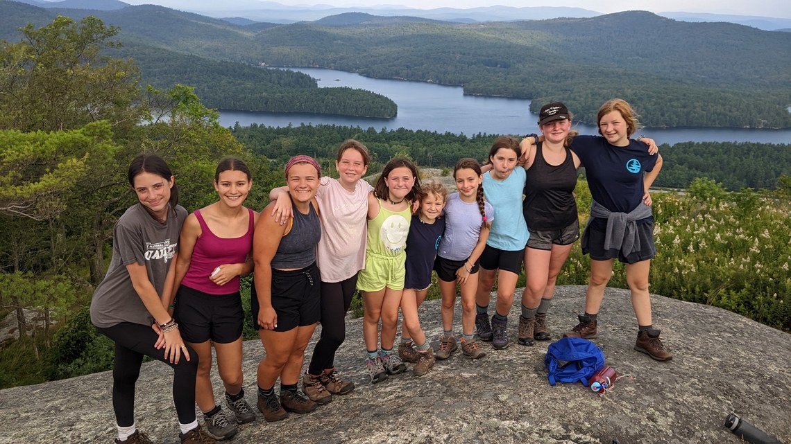 A group of girls smiling on top of a mountain