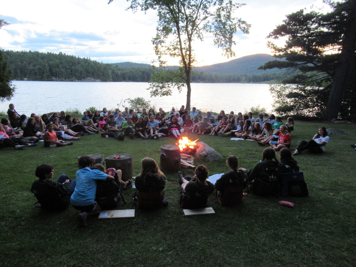 All of the campers and counselors sitting on the side of the lake singing songs on the last night of camp