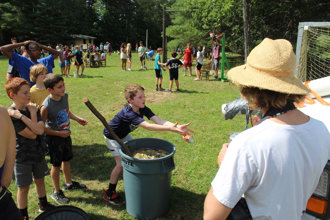 A camper trying to catch a can of soda before it falls into a bucket of slime