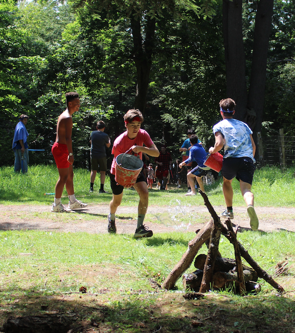 Two teams of campers competing in a race to see who can put out a fire first with buckets of water