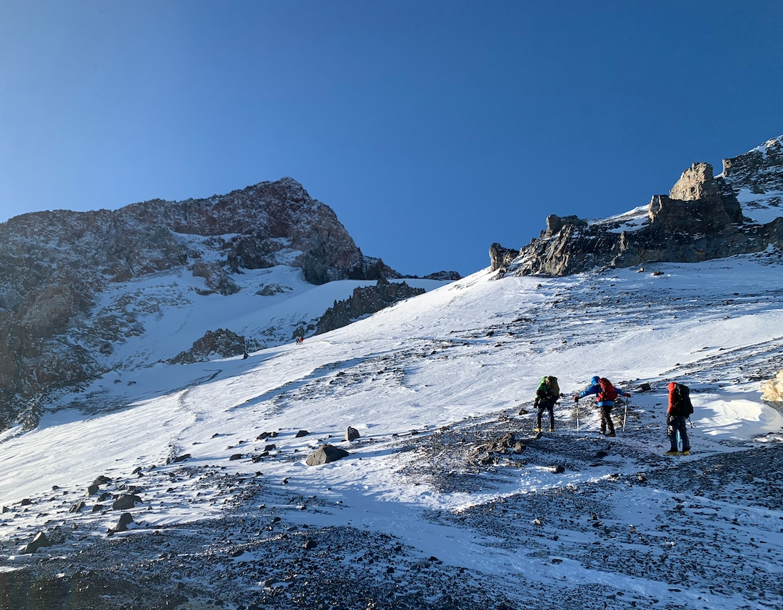 A group of three hikers seen from far away as they begin the rocky trek toward Aconcagua mountain