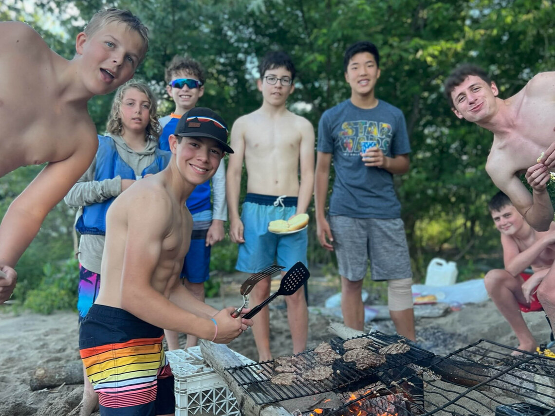 campers gathered around a firepit cooking burgers