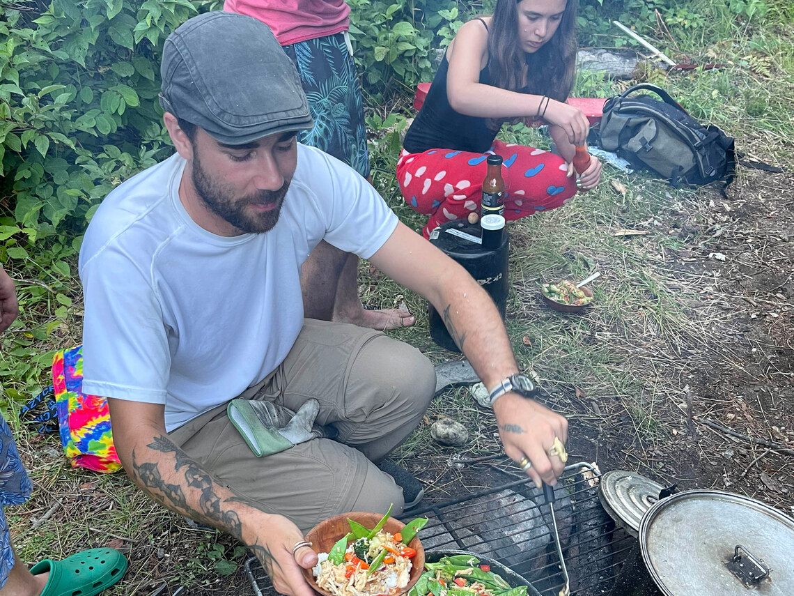 a counselor cooking stir fry over a camping stove in the woods