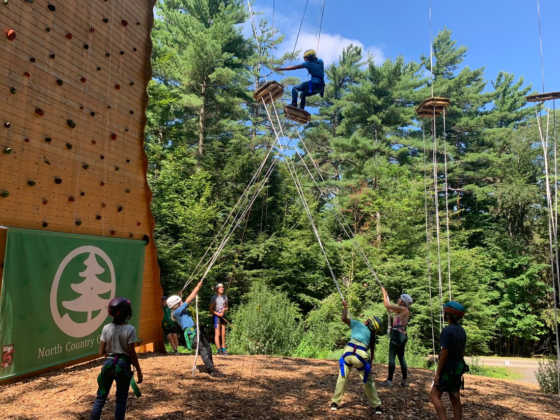 a group of campers watching another crossing a high element in a ropes course