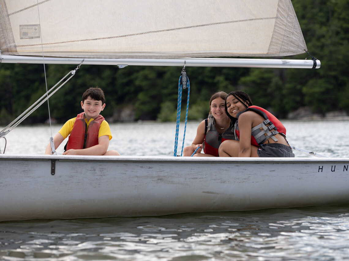 three campers smiling in a sailboat