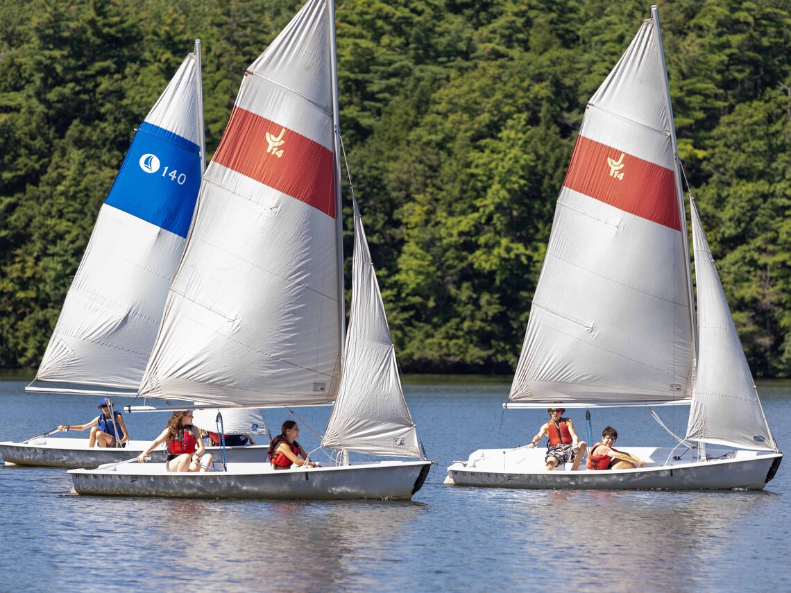 three sailboats being sailed by campers on a lake