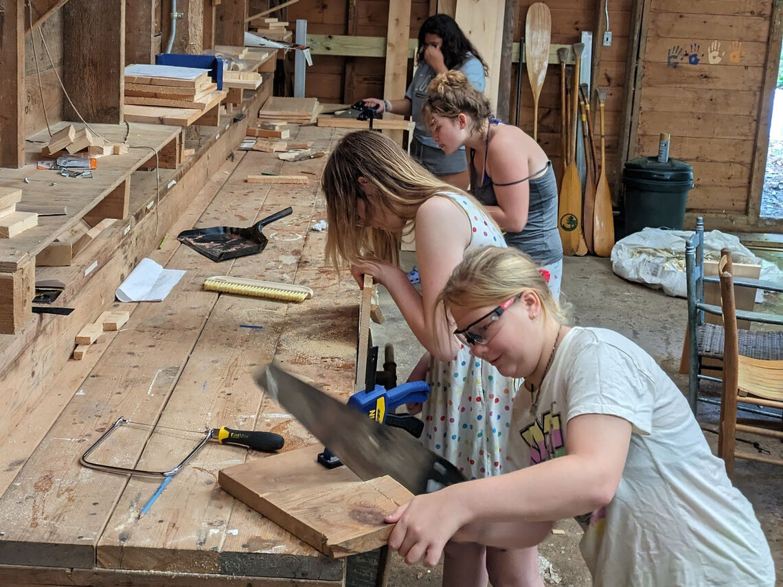 campers lined up at a worktable all sawing pieces of wood
