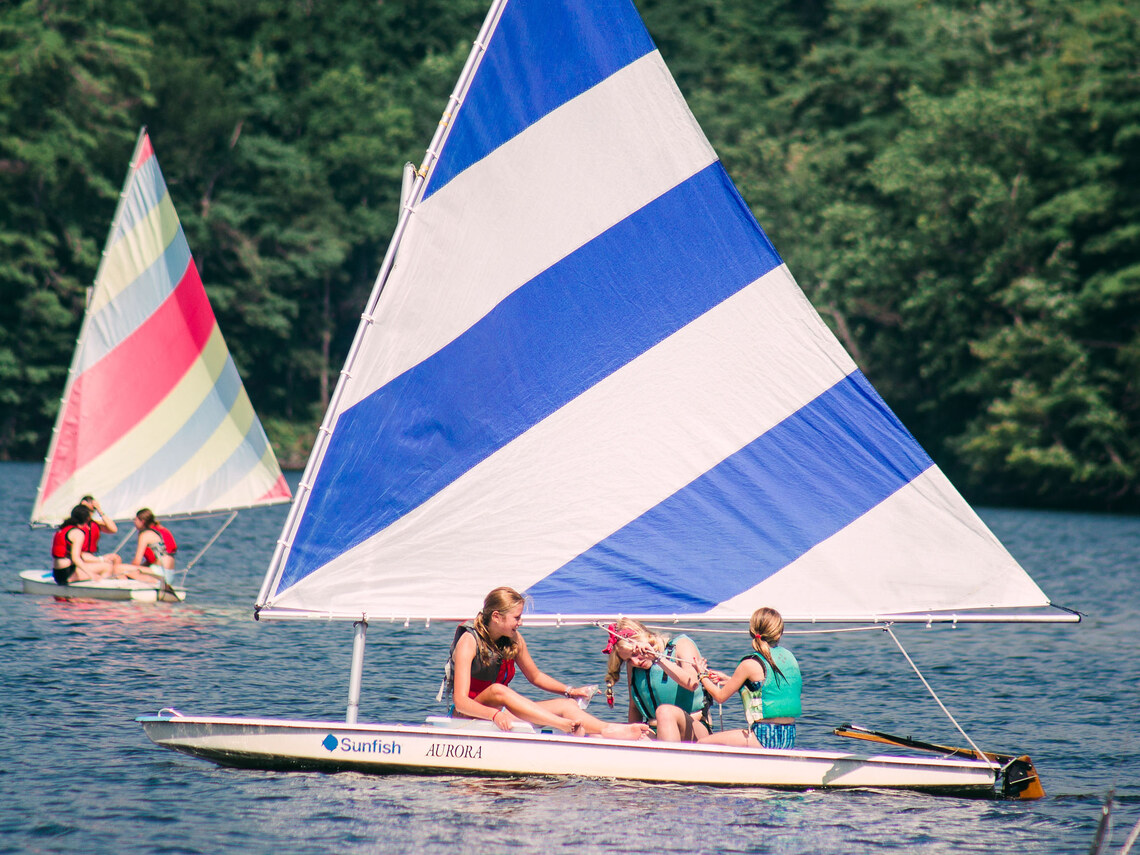 two brightly colored sailboats being sailed by campers