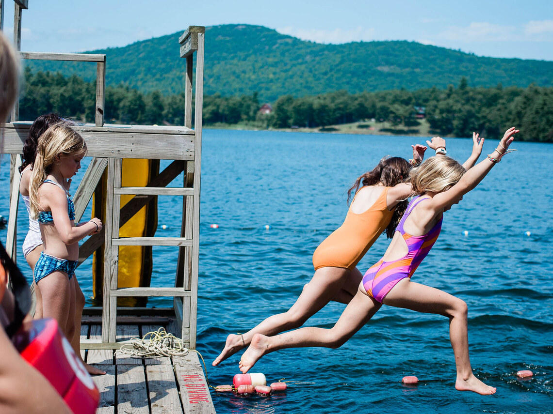 two campers leaping off of a dock into the water