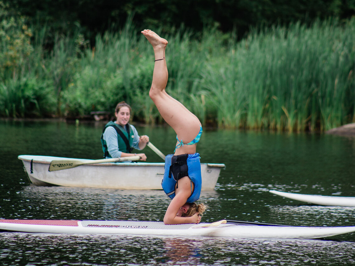 a counselor doing a headstand on a paddleboard