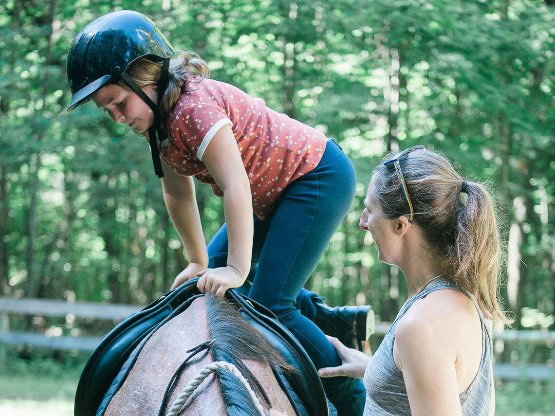 a counselor helping a camper to get on a horse