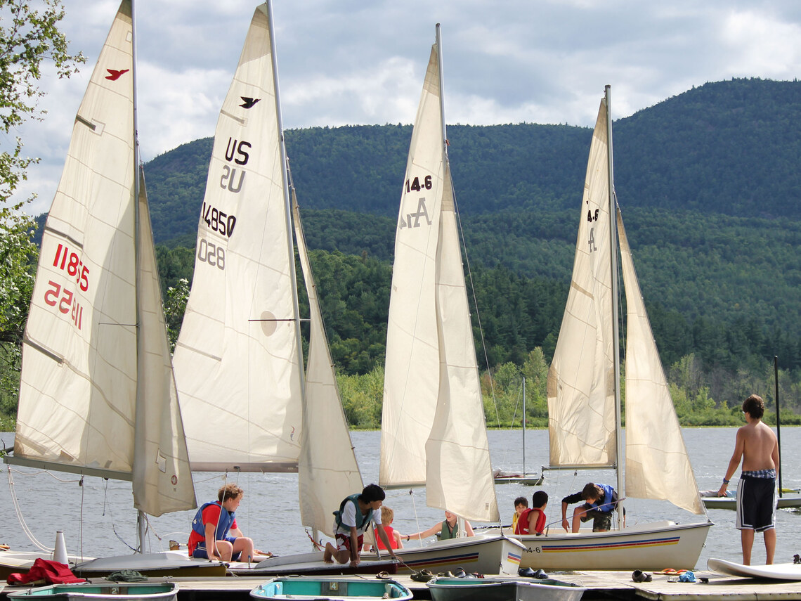 many sailboats lined up on the side of a dock with lots of campers in and around them