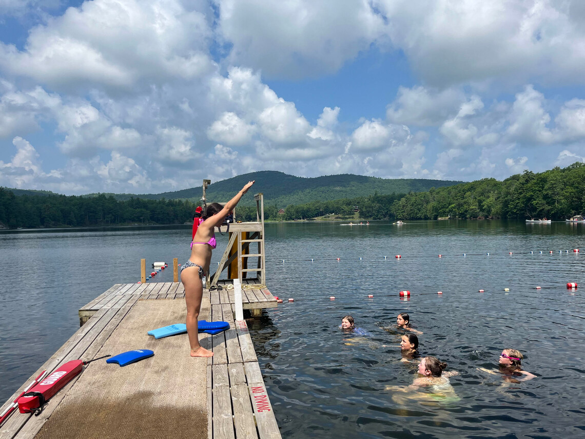 a counselor demonstrating how to do correct swim strokes to a group of campers in the water