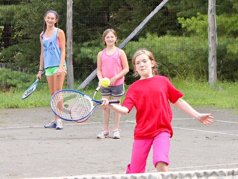 girls learning to play tennis on court