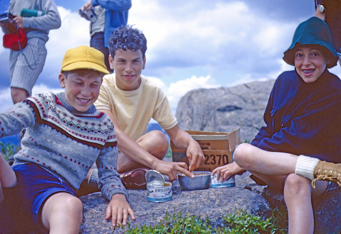 Boys eating tuna out of cans on top of a mountain