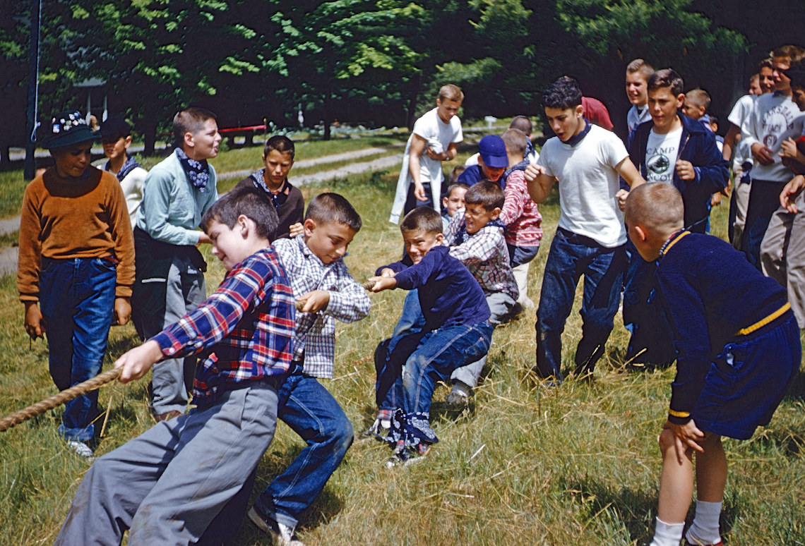 boys playing tug of war with their friends cheering around them