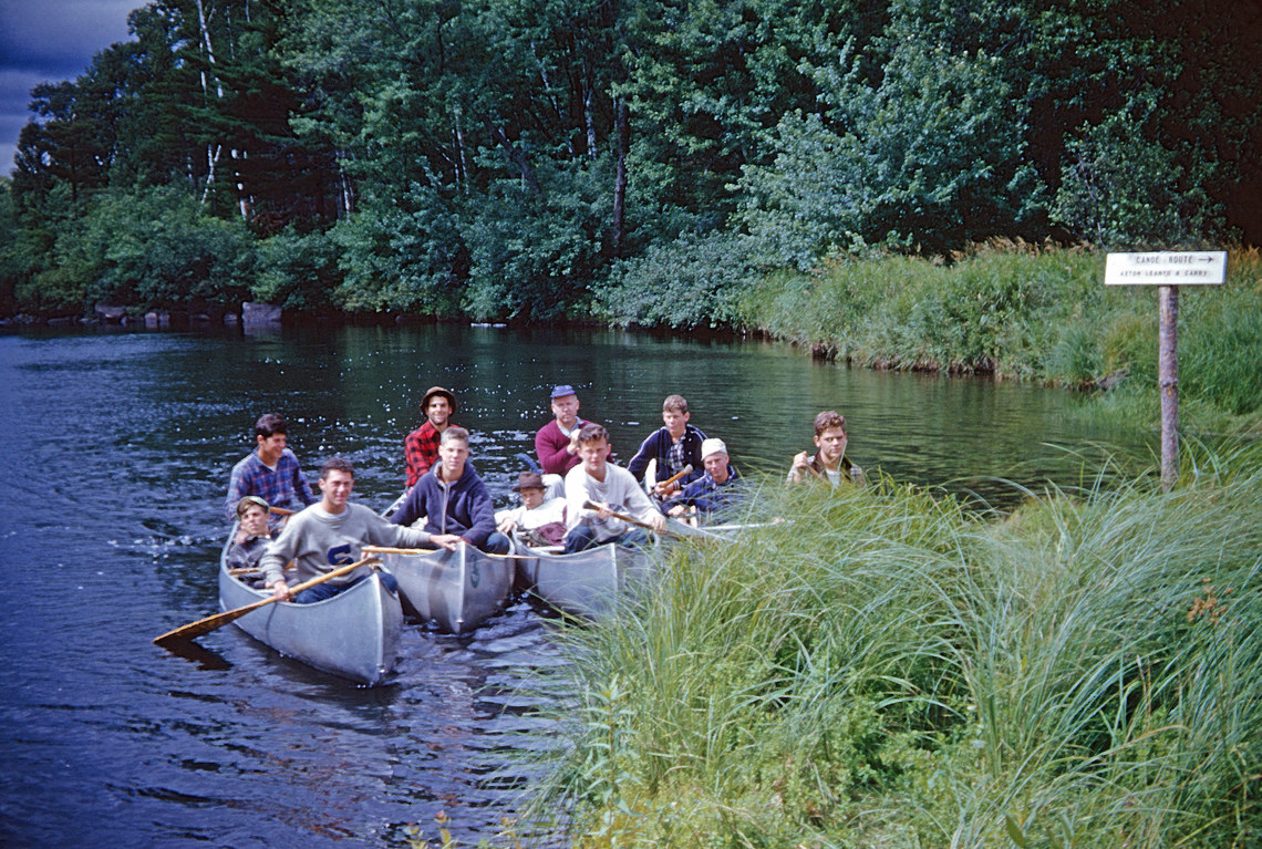 Campers and counselors in canoes that are all docked in a row