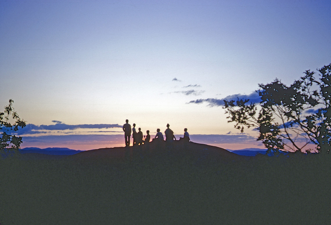 Silhouettes of a group of people standing on the top of a mountain with the colors of the sunset around them