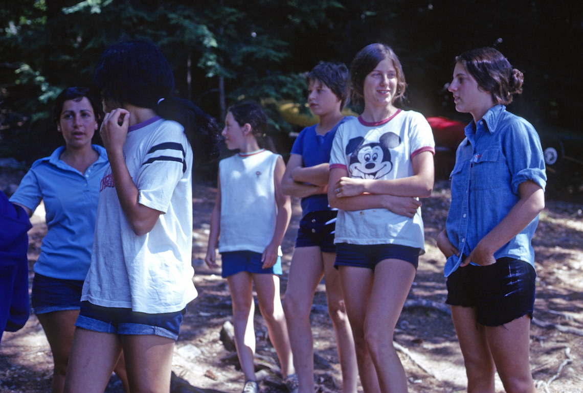 A group of campers standing in the woods talking to friends