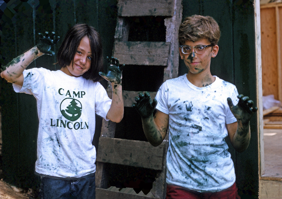 Two kids smiling for the camera with green paint all over their hands and clothes
