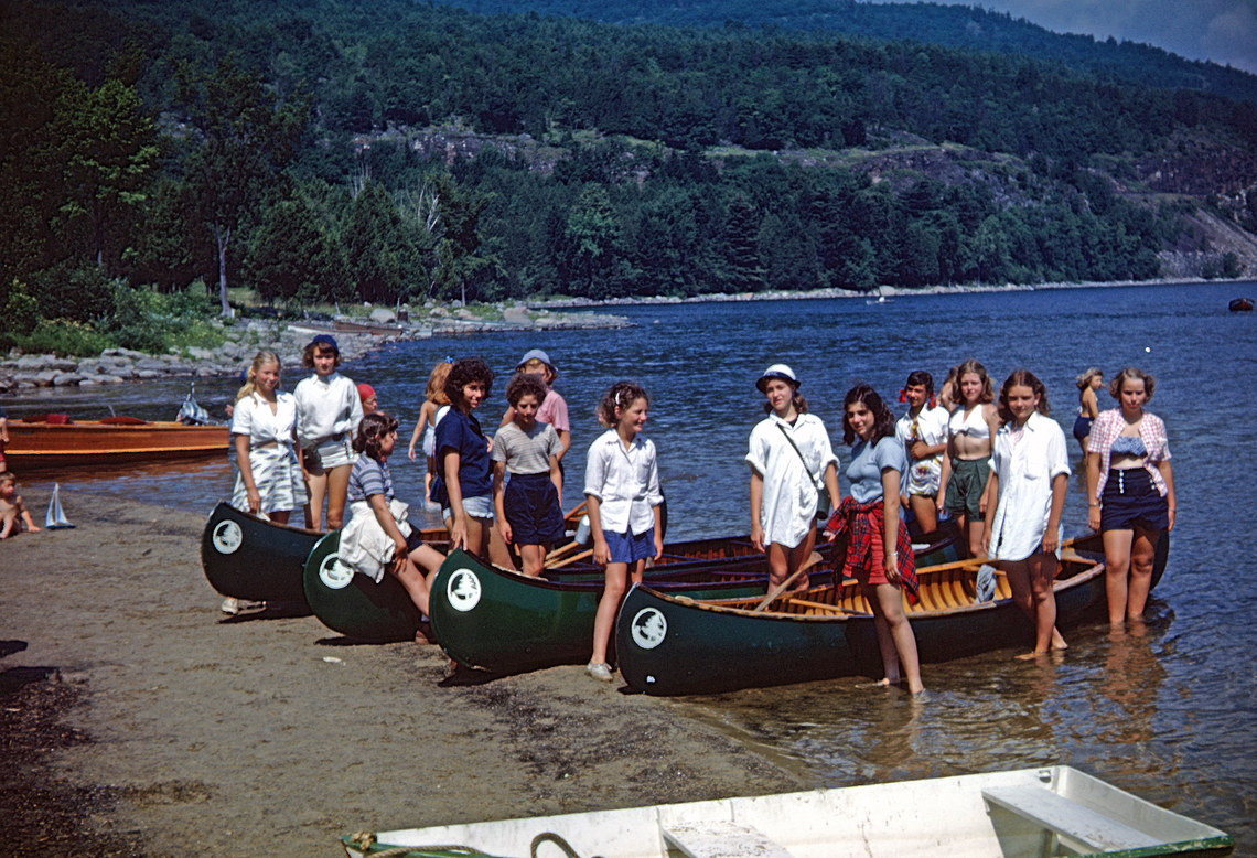 A group of campers standing around their wooden canoes on lake champlain