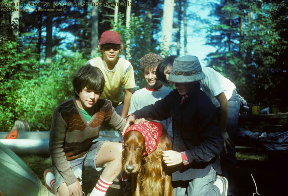 A group of boys standing around a dog that is wearing a red bandana on it's head