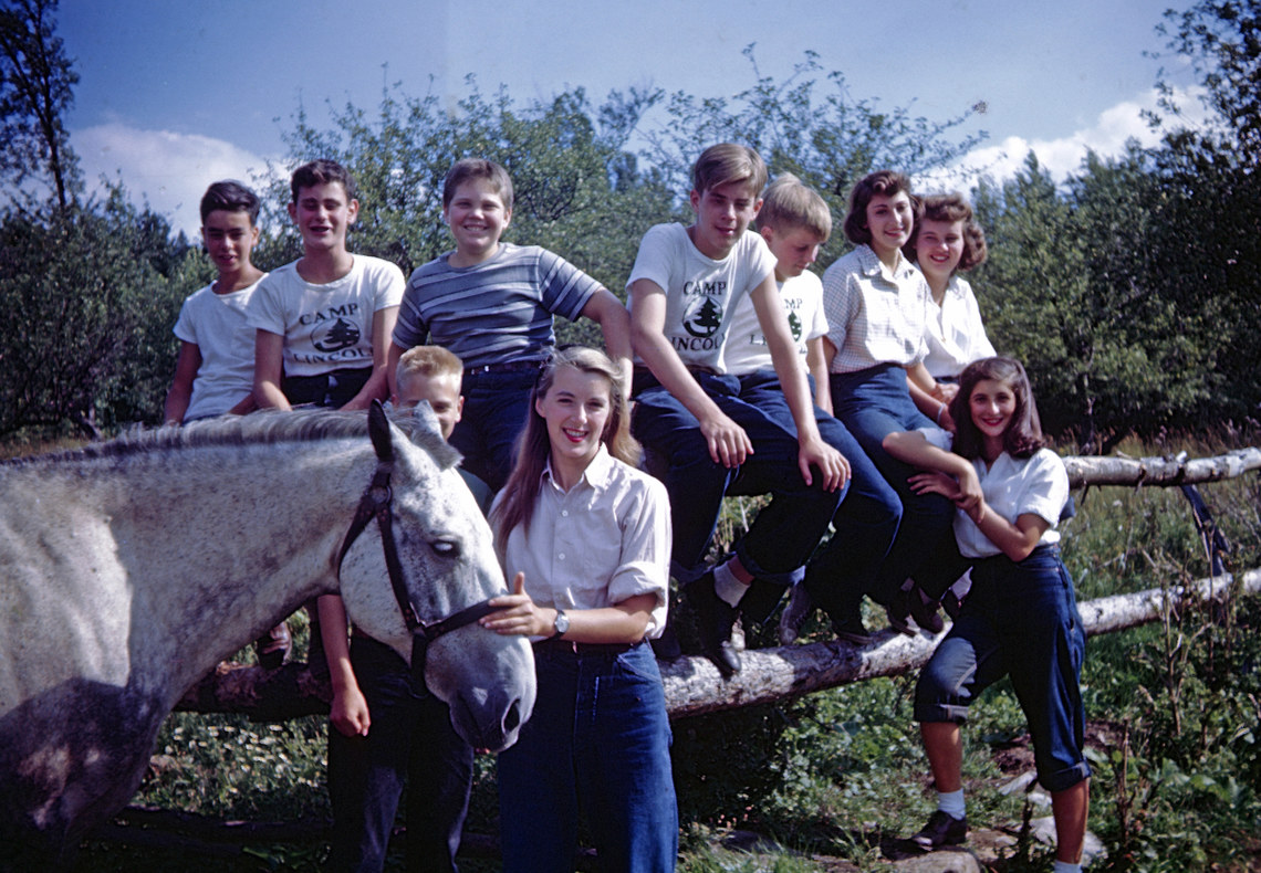Campers sitting on a wooden fence with a counselor and horse in the foreground