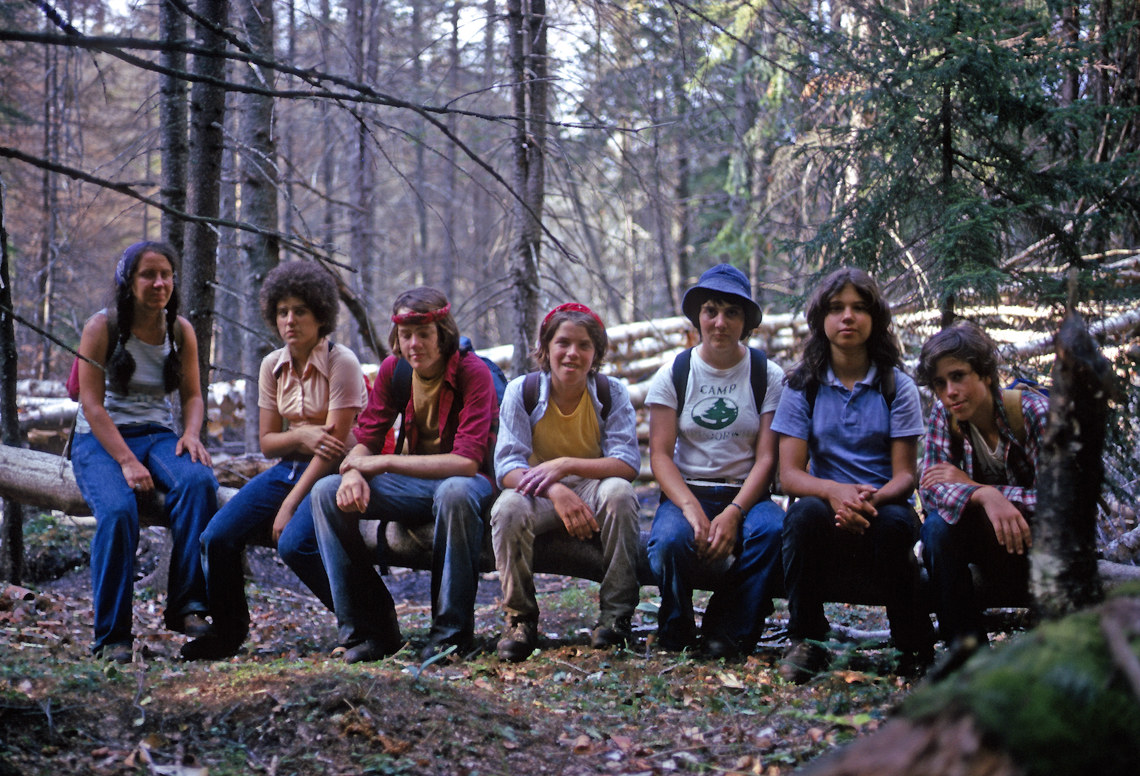 A group of girls in backpacks sitting on a fallen tree during a hike