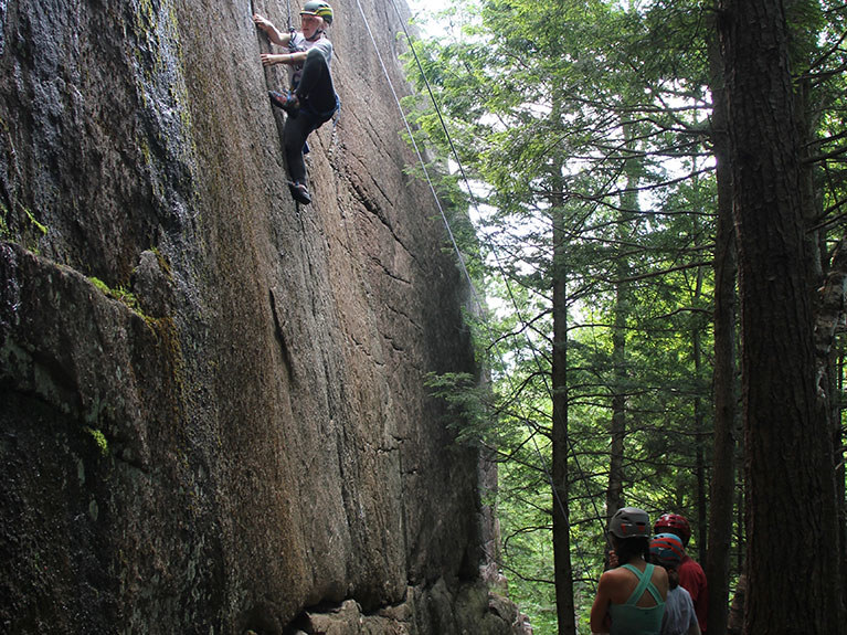 camper rock climbing with other campers spotting below